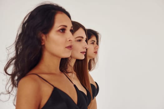 Side view. Three young women in lingerie together indoors. White background.