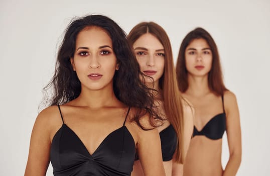 In black bra. Three young women in lingerie together indoors. White background.