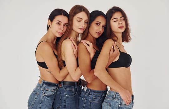 Leaning on each other. Four young women in lingerie together indoors. White background.
