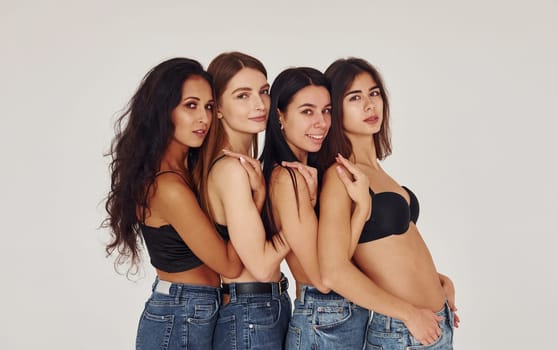 Leaning on each other. Four young women in lingerie together indoors. White background.