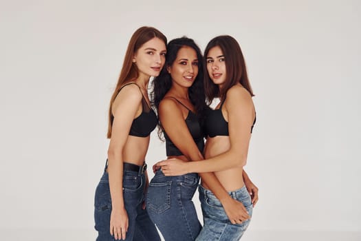 Embracing each other. Three young women in lingerie together indoors. White background.