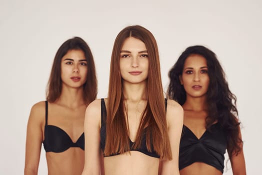 Three young women in lingerie together indoors. White background.