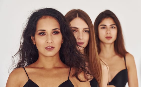 Three young women in lingerie together indoors. White background.