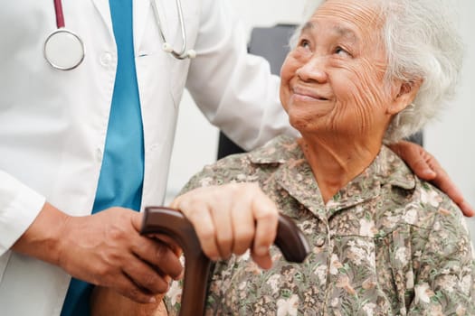 Doctor help Asian elderly disability woman patient holding walking stick in wrinkled hand at hospital.