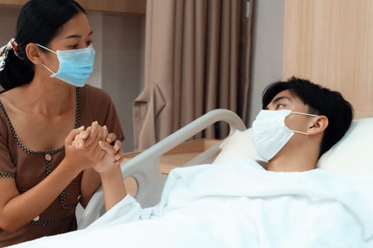 Young patient with attentive visitor and family holding hands in hospital sterile recovery room. The concept of family support for patients receiving hospital care. In-ward medical care and healthcare