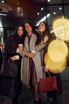 Cups of drink in hands. Three cheerful women spends Christmas holidays together outdoors. Conception of new year.