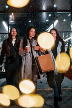 Cups of drink in hands. Three cheerful women spends Christmas holidays together outdoors. Conception of new year.