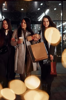 Cups of drink in hands. Three cheerful women spends Christmas holidays together outdoors. Conception of new year.