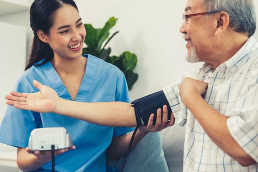 A contented retired man having a blood pressure check by his personal caregiver at his home with a smiley face. Senior care at home, nursing home for pensioners.