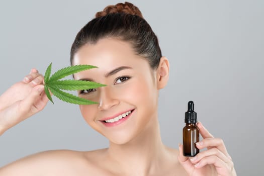 Glamorous beauty portrait of beautiful young woman with flawless clean skin cosmetic makeup holding cannabis green leaf, CBD extracted oil bottle for natural skincare treatment in isolated background.