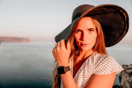 Portrait of happy young woman wearing summer black hat with large brim at beach on sunset. Closeup face of attractive girl with black straw hat. Happy young woman smiling and looking at camera at sea