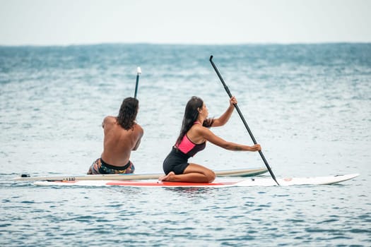 Sea woman and man on sup. Silhouette of happy young woman and man, surfing on SUP board, confident paddling through water surface. Idyllic sunset. Active lifestyle at sea or river