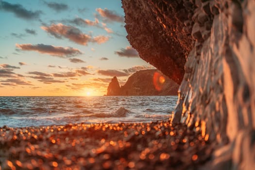 Sea sunset waves with foam. Waves run on pebbles and rock from volcanic basalt. Water breaks into splashes and white foam. Against the background of the cape and the sunset sky