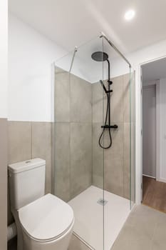 An empty tiny bathroom with a toilet and a glazed shower with gray tiles. The concept of a simple and stylish bathroom in an apartment or luxury hotel.