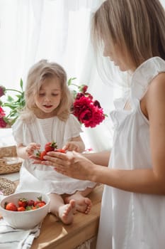 A little blonde girl with her mom on a kitchen countertop decorated with peonies. The concept of the relationship between mother and daughter. Spring atmosphere