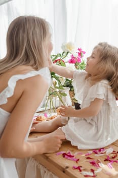 A little blonde girl with her mom on a kitchen countertop decorated with peonies. The concept of the relationship between mother and daughter. Spring atmosphere