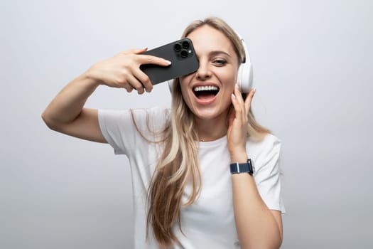 girl makes a face in wireless headphones with a smartphone in her hands on a white background.