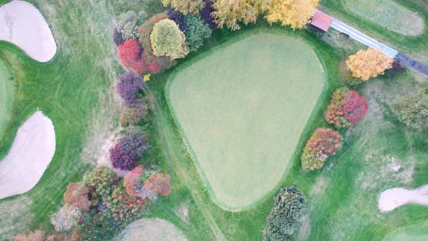 Golf courses among yellow-red autumn trees. Drone view of the river, green grass, willow and golden leaves of trees. Paths for golf cars. Wheel tracks. Beautiful landscape of the park. Kazakhstan