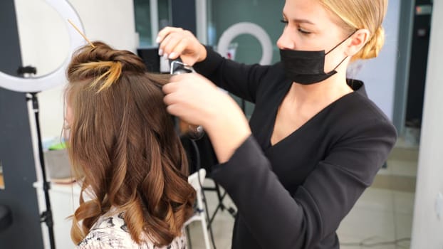 The hairdresser curls the girl's hair in a beauty salon