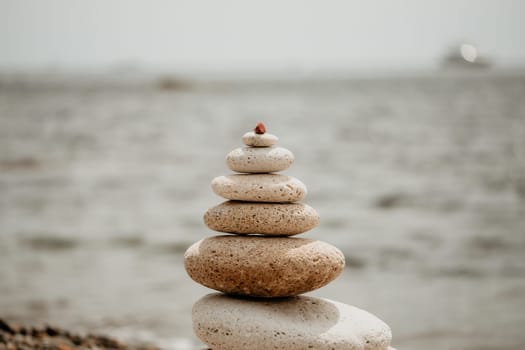 Pyramid stones on the seashore with warm sunset on the sea background. Happy holidays. Pebble beach, calm sea, travel destination. Concept of happy vacation on the sea, meditation, spa, calmness.