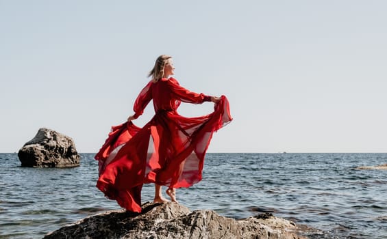 Woman travel sea. Young Happy woman in a long red dress posing on a beach near the sea on background of volcanic rocks, like in Iceland, sharing travel adventure journey