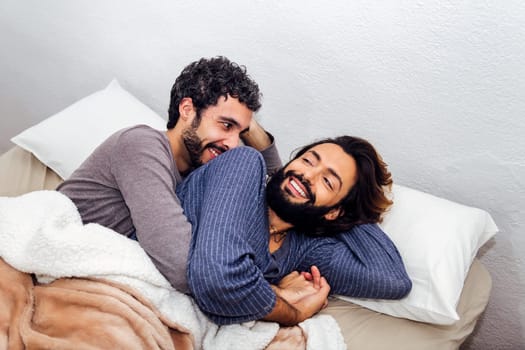 gay male couple cuddling in bed happy to wake up together in the morning, concept of real people lifestyle and love between people of the same sex