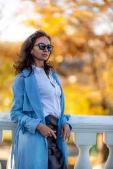 Woman autumn city, lifestyle. A middle-aged woman in a blue raincoat, black leather skirt and white blouse walks through the autumn city