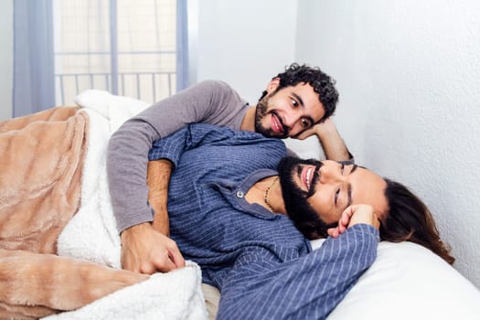 gay male couple relaxing together at bed and smiling happy in the morning, concept of real people lifestyle and love between people of the same sex