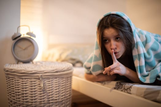 A sleep-deprived woman wants to silence her loud alarm clock. Bedroom in bright colors. A girl under a soft blanket.