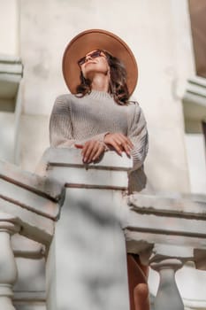 Woman walks in the city, lifestyle. Young beautiful woman in a loose light sweater, brown skirt and sneakers with a hat