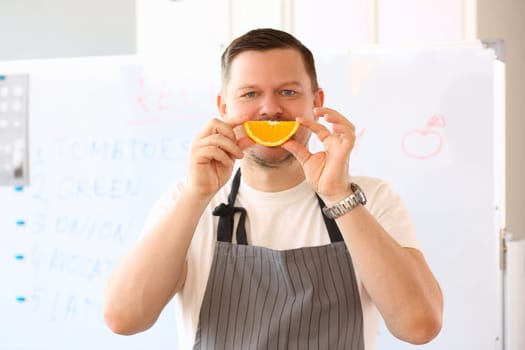 Emotionally smiling male cook holds an orange slice together smiles. Vitamin c and health concept