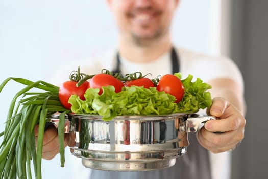 Cook is holding salad of tomatoes and green onions in saucepan. Improving health through nutrition and vitamins concept