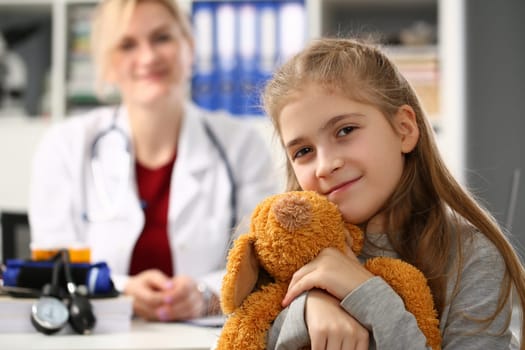 Little girl holding bear toy at medical appointment with pediatrician. Children doctor and child examination concept