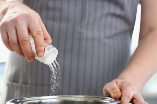 Hands of cook man salts water in saucepan in kitchen. Dose of salt in meals concept
