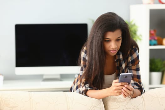 African woman chatting at home using smartphone. Black woman reading news in phone concept