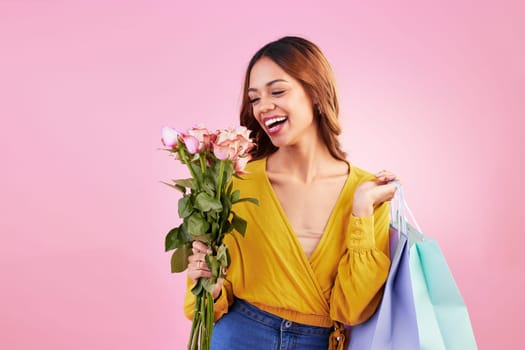 Happy, shopping bags and smile with woman and flowers in studio for retail, birthday and spring. Event, party and celebration with female and roses on pink background for sale, discount and romance.