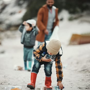 Beach clean, plastic and pollution with a child cleaning the environment for dirt or bottle on sand. Male kid and family walking as volunteer for sustainability, community service and global warming.