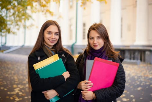 Portrait of two beautiful girls students near university building at Autumn