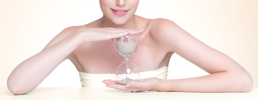 Closeup personable model holding hourglass in beauty concept of anti-aging skincare treatment. Young girl portrait with perfect smooth clean skin and flawless soft makeup in isolated background