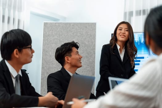 Confidence and young asian businesswoman give presentation on financial business strategy in dashboard report display on screen to colleagues in conference room meeting as harmony in workplace concept