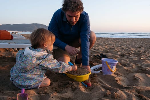 Father and child sitting at the beach in the sunset making sand castles