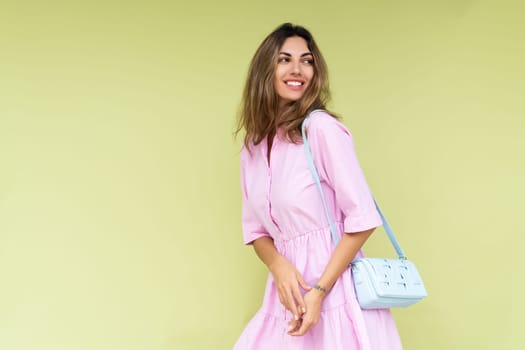 Young woman in casual pink summer cotton dress wear isolated on green background holding cute blue shoulder bag happy big smile