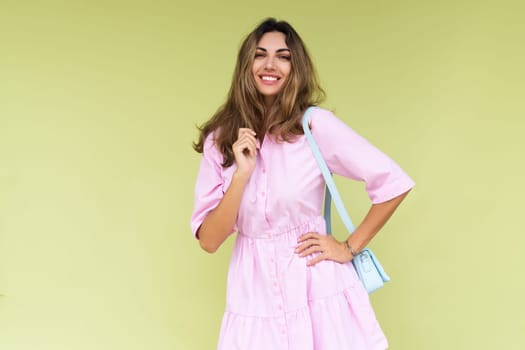 Young woman in casual pink summer cotton dress wear isolated on green background holding cute blue shoulder bag happy big smile