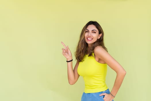 Young brunette in casual wear isolated on green background happy look to camera smile excited point finger to left