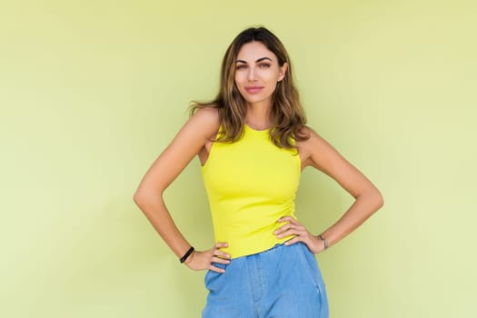 Young brunette in casual wear isolated on green background happy look to camera with natural confident calm smile