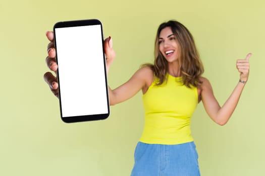 Young woman in casual wear isolated on green background holds a phone with a blank white screen