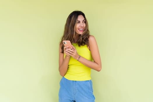 Young woman in casual wear isolated on green background holding phone and look aside with big smile