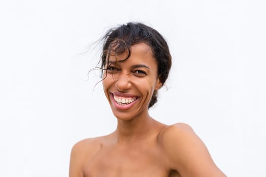 Beauty portrait of young topless african american woman with bare shoulders on white background with perfect skin and natural makeup positive laughing