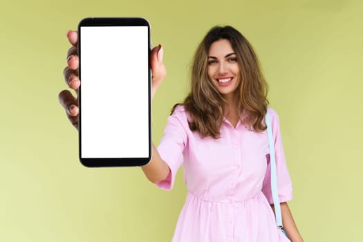 Young woman in casual wear isolated on green background holds a phone with a blank white screen