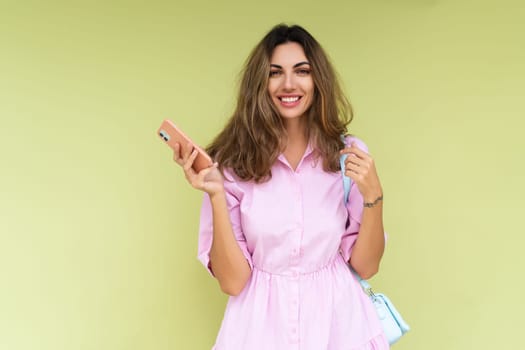 Young woman in casual wear isolated on green background holding phone and look to camera with a big natural smile